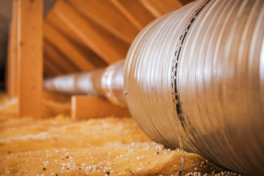 Metal ducting is placed in an attic with insulation around it for air circulation.