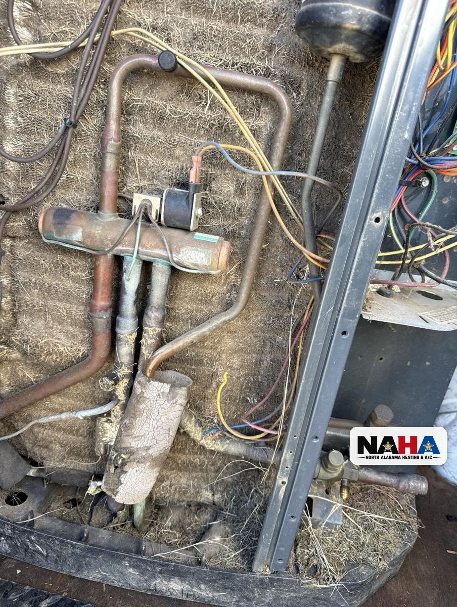 Inside an old outdoor AC unit in South Huntsville with corroded copper lines, cracked insulation and packed debris