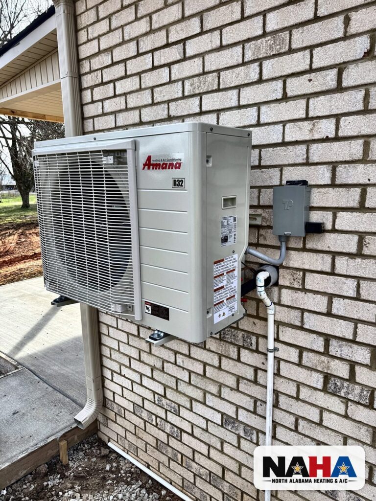 Side discharge heat pump mounted on a brick wall, installed by North Alabama Heating & A/C